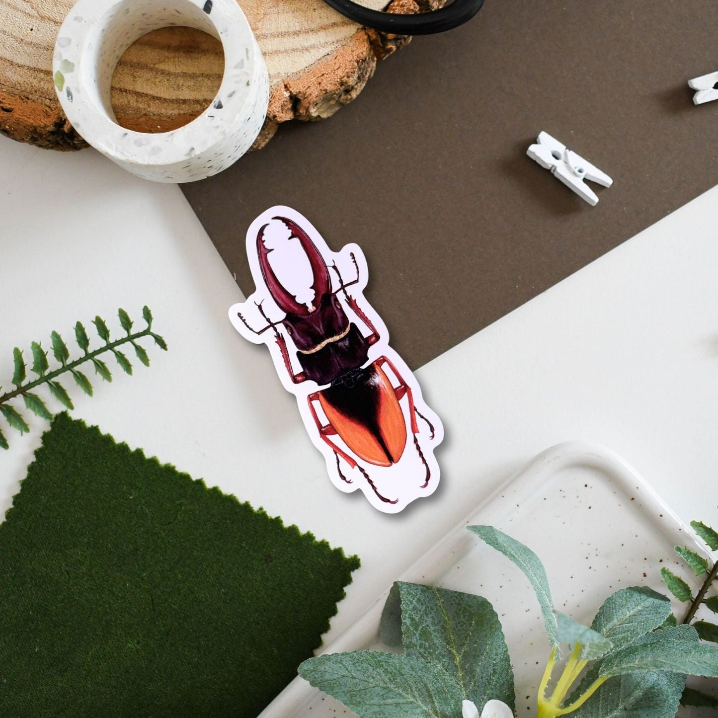 Sticker of a scarab beetle on a surface with plants and a wooden block.