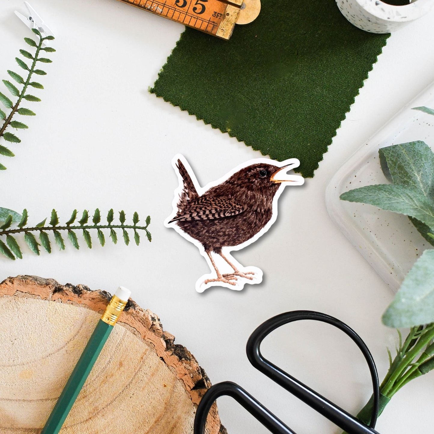 Sticker of a bird with a ruler, green fabric, and scissors on a white surface