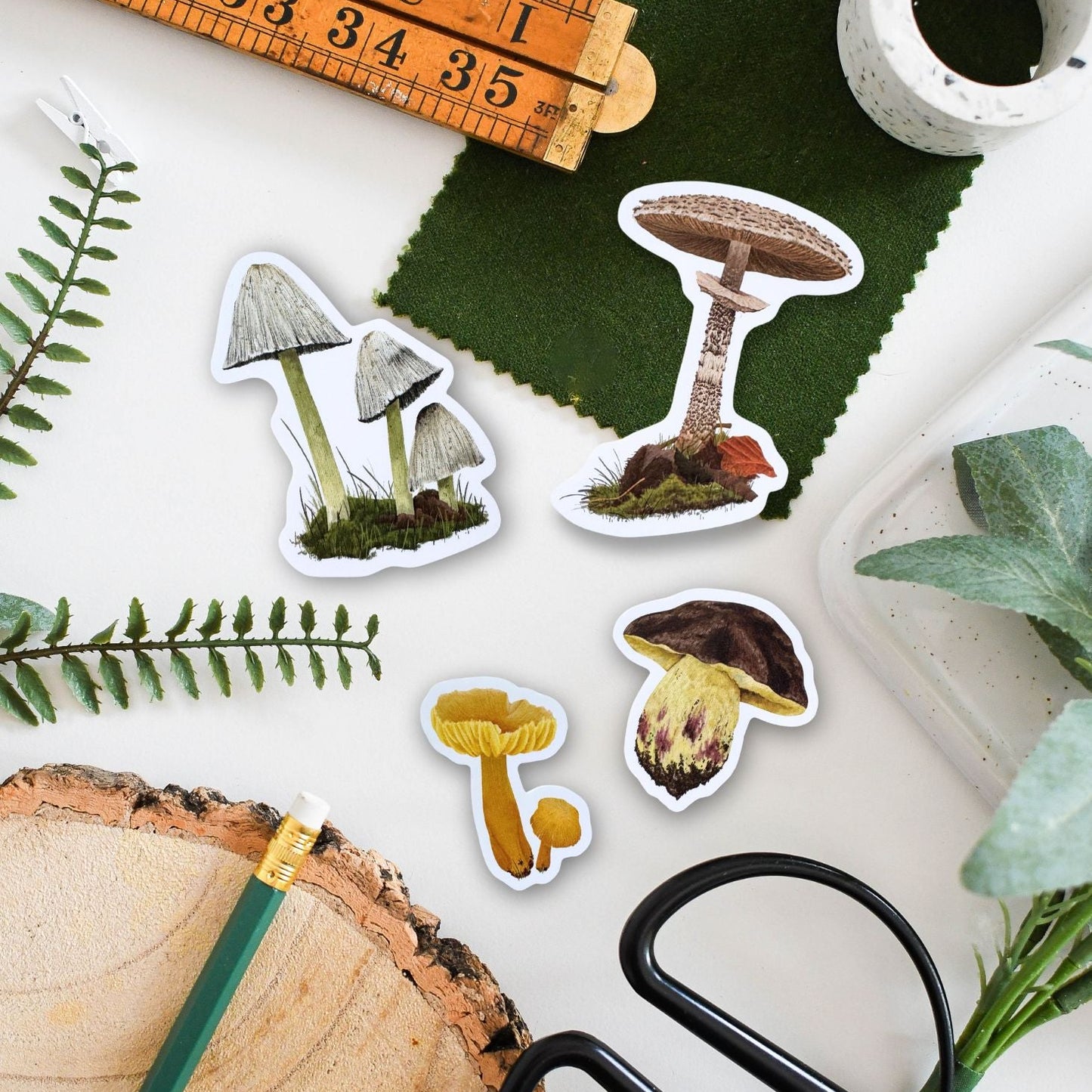 Mushroom-themed stickers on a surface with a ruler, scissors, and natural elements.