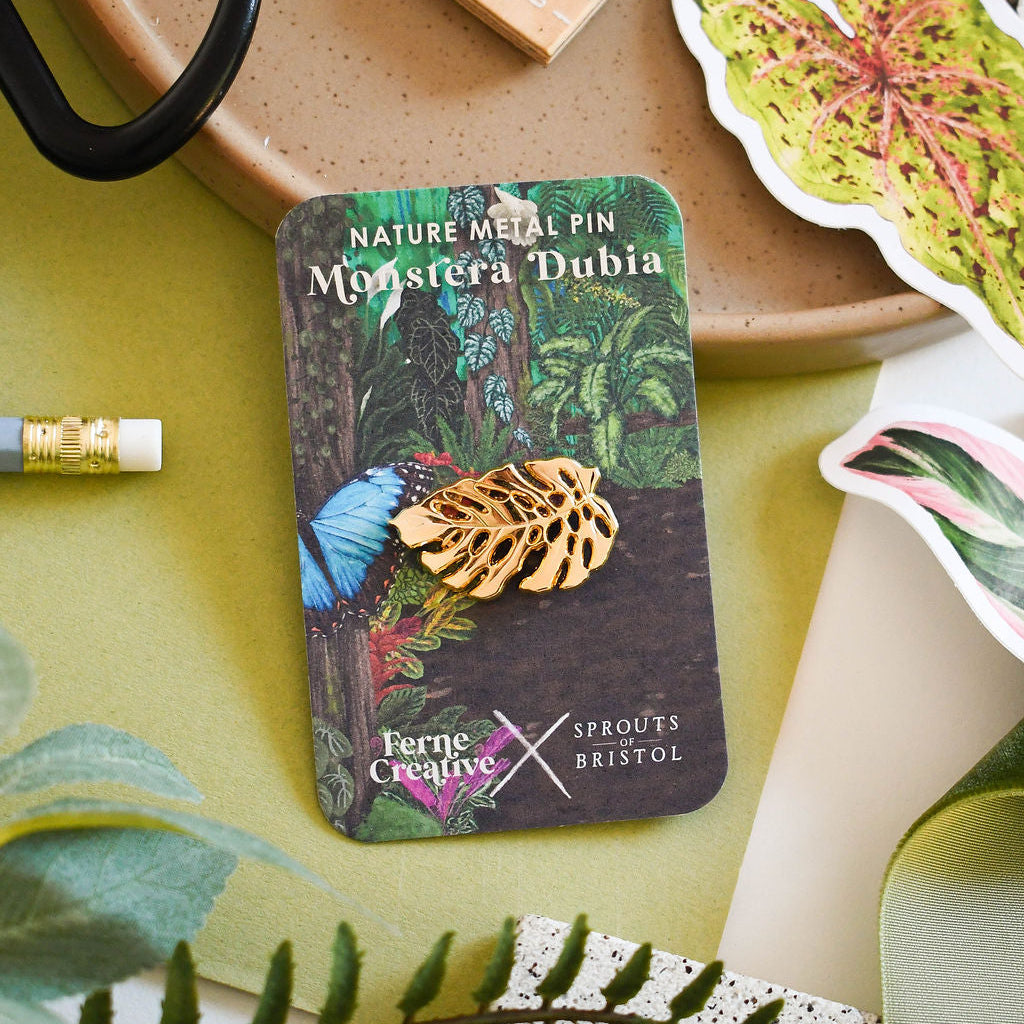 Gold leaf nature metal pin on a branded card with decorative elements on a table.