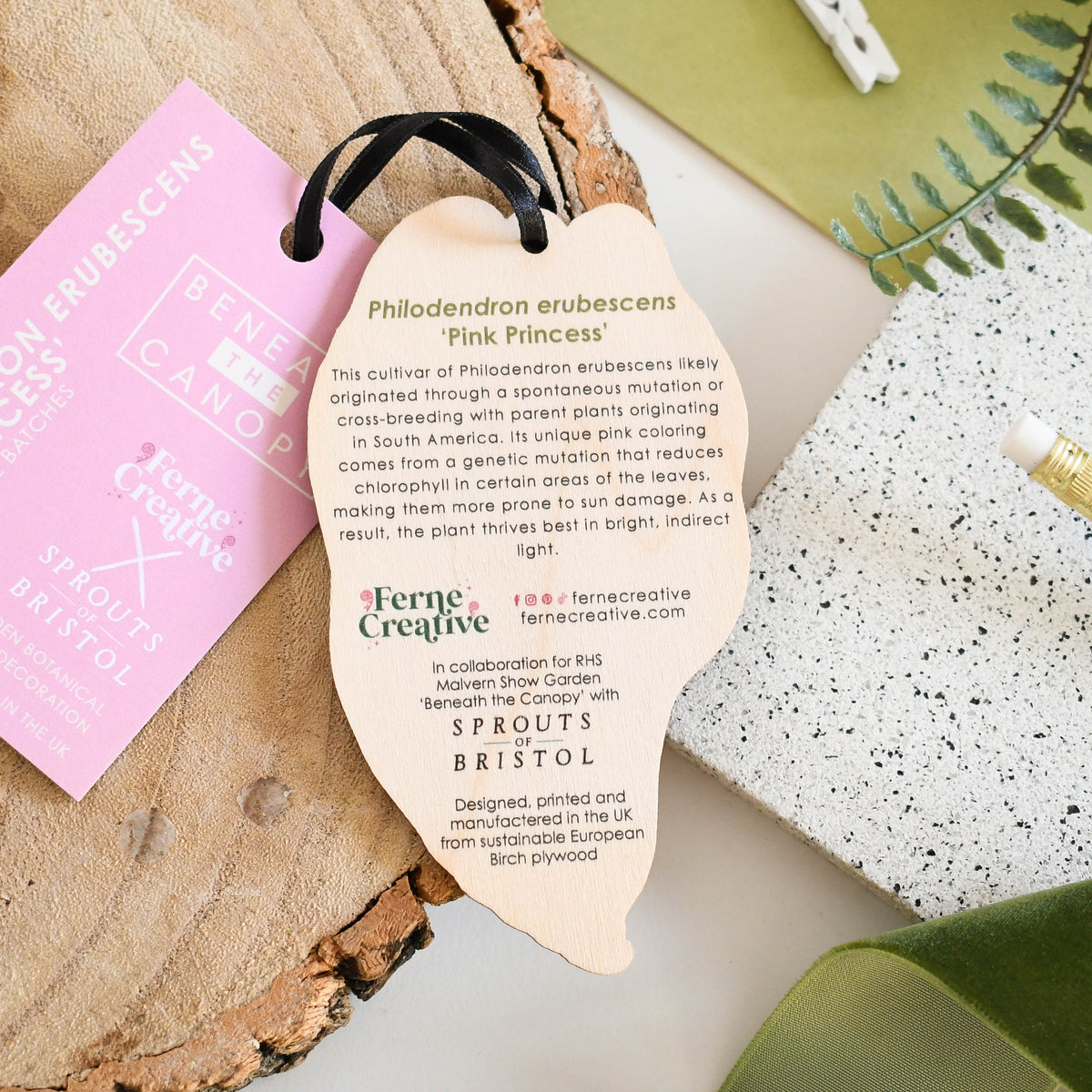 Heart-shaped plant decoration on a wooden surface with a pink tag and greenery.