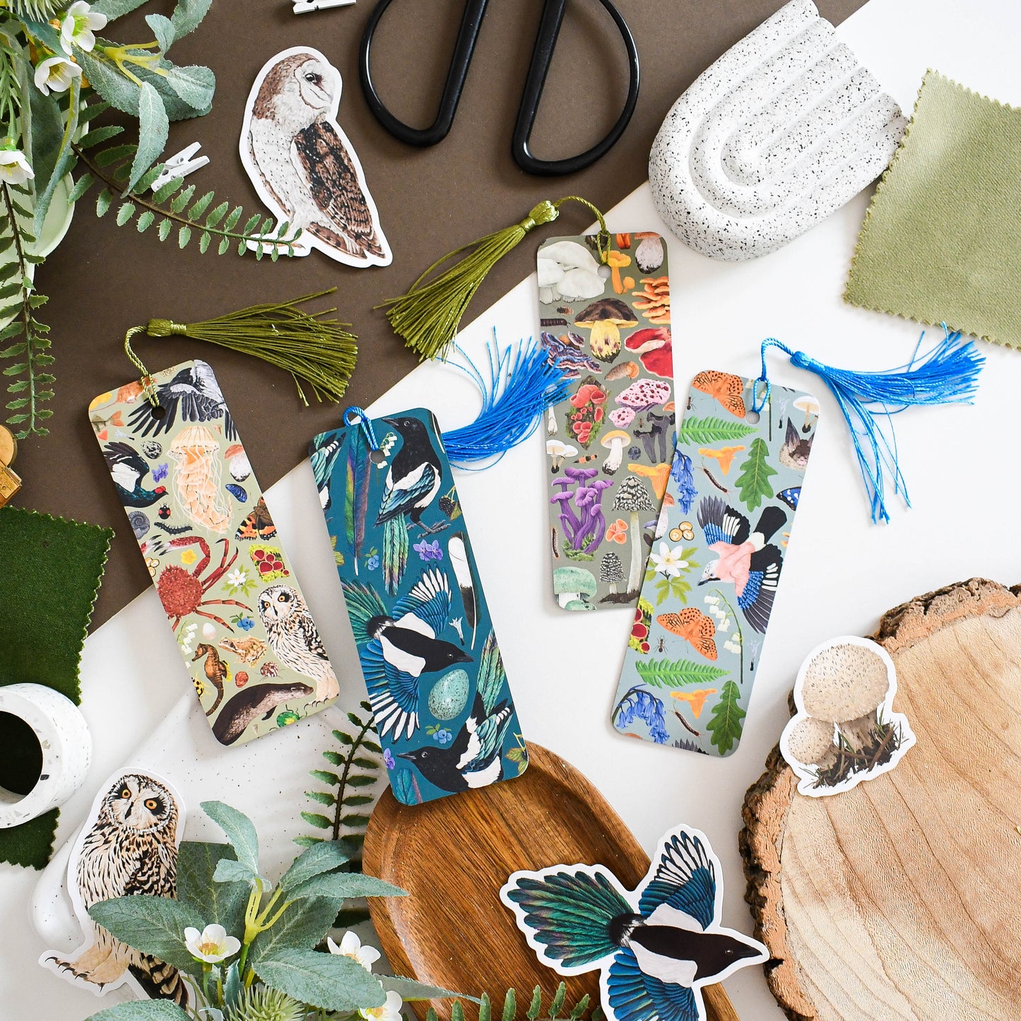 Colorful nature-themed bookmarks and decorative items on a wooden surface with plants and scissors.