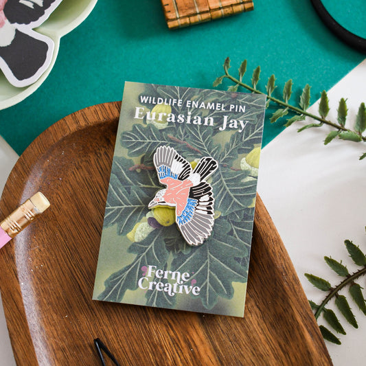 Enamel pin of Eurasian Jay on a illustrated Oak Tree card with 'Ferne Creative' branding, placed on a wooden tray.