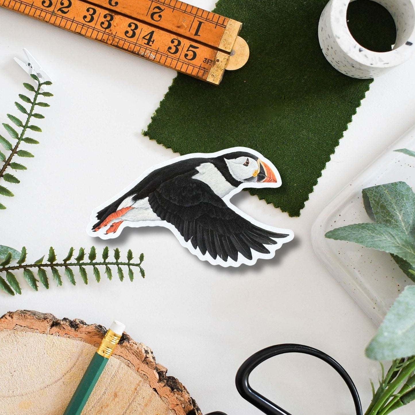 Puffin sticker on a surface with a ruler, scissors, and natural elements