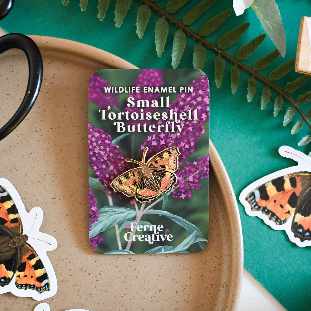 Small Tortoiseshell Butterfly enamel pin on a card with greenery and butterfly stickers in the background