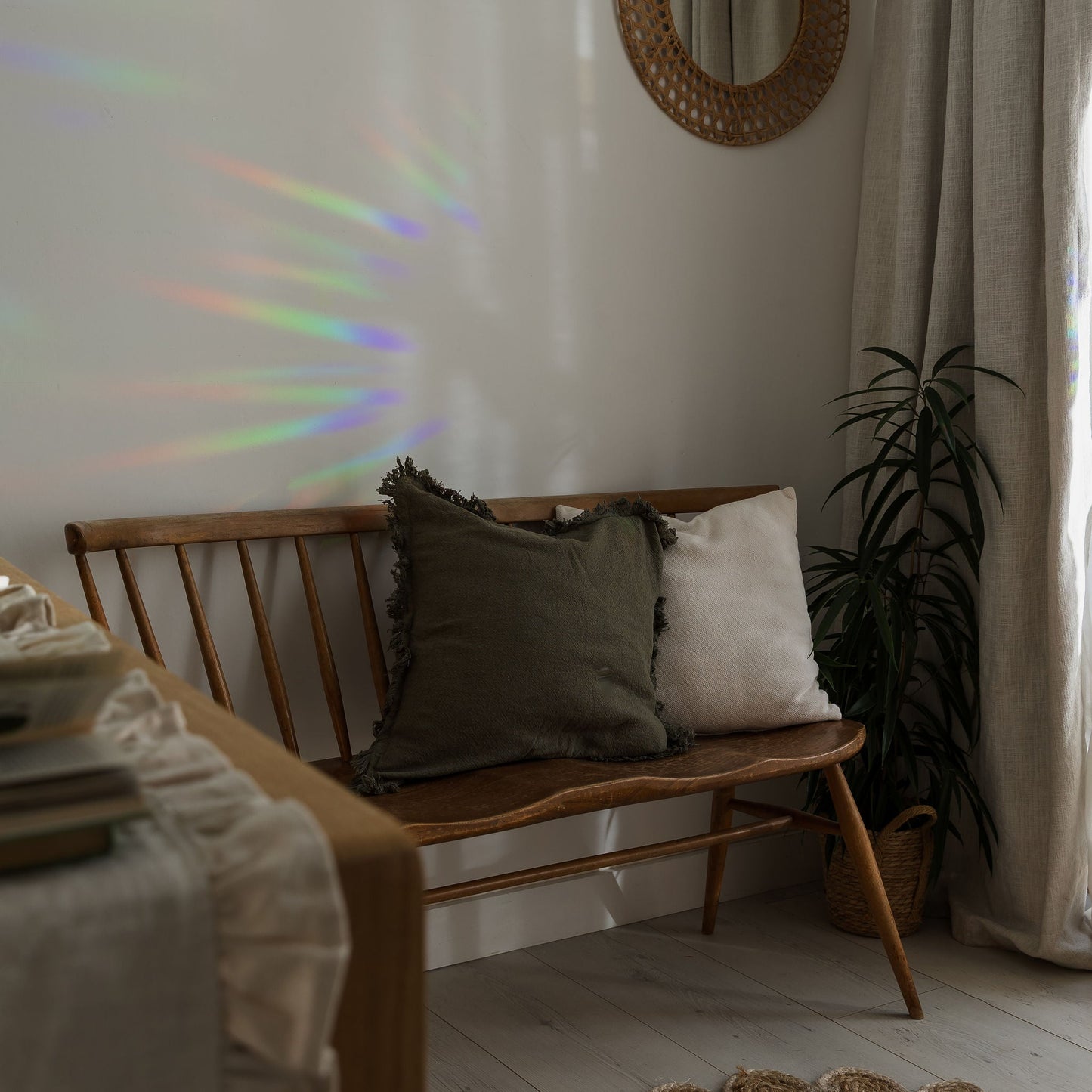 Wooden bench with cushions against a wall with a round mirror and plant
