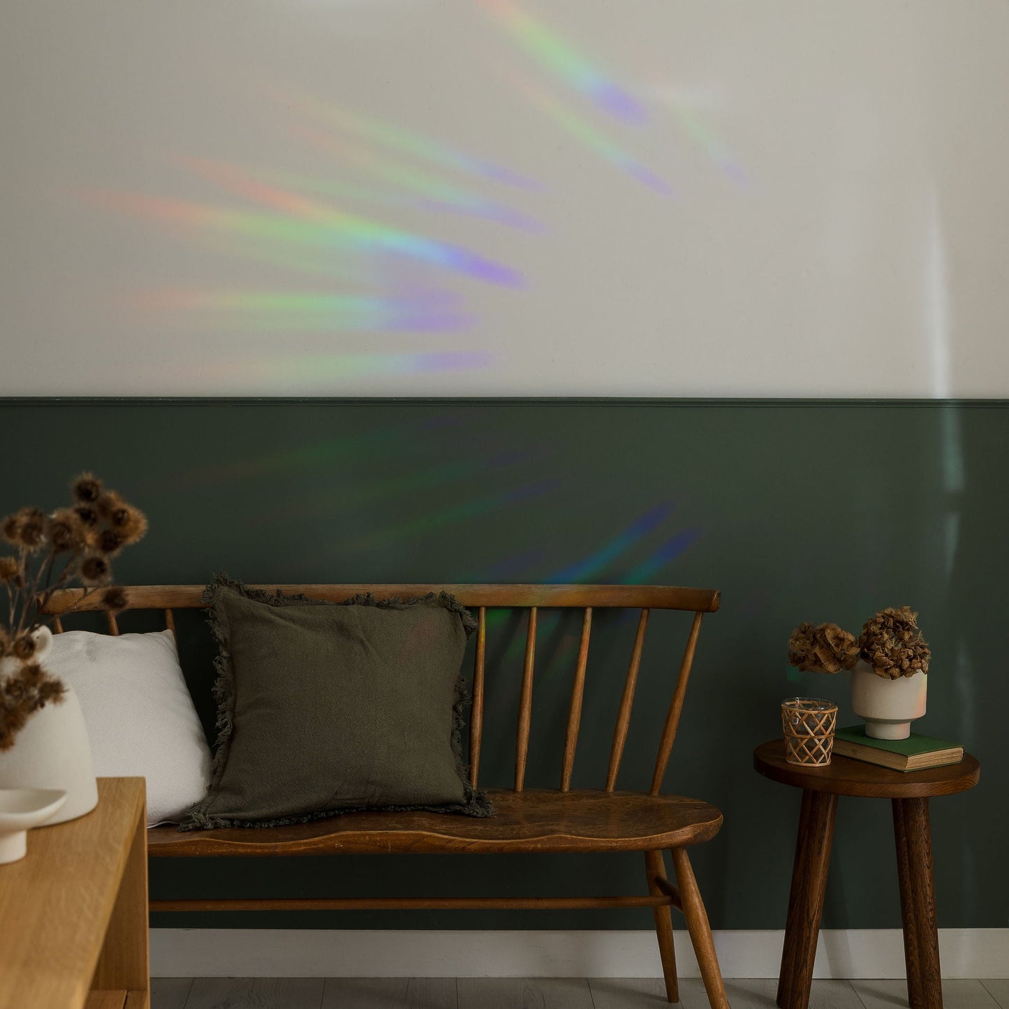 Wooden bench against a green wall with a rainbow projection, in a room with a side table and decor items.
