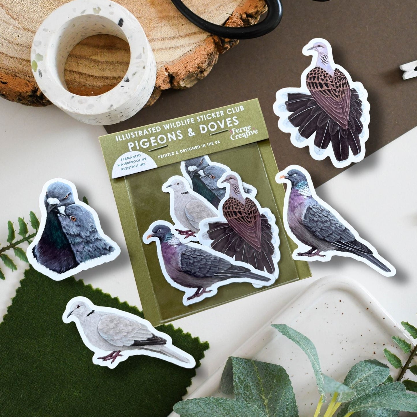 Pack of illustrated stickers with pigeons and doves on a wooden surface with plants.