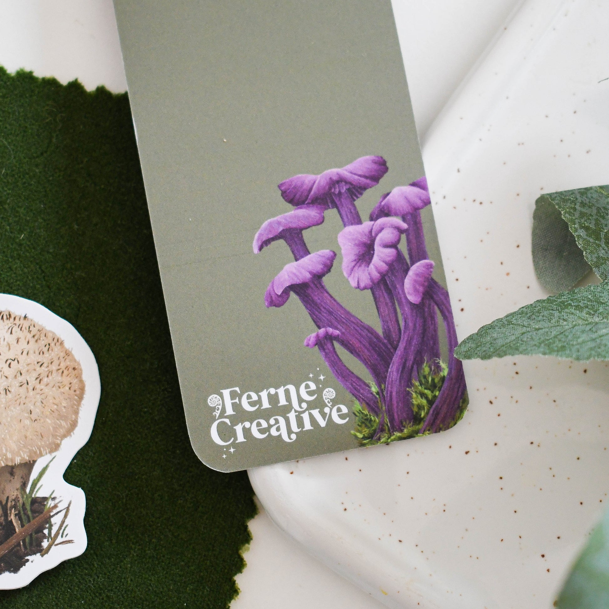 Purple mushroom illustration on a green card with 'Ferne Creative' branding, surrounded by greenery.
