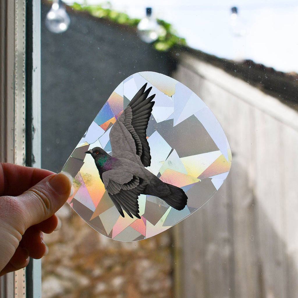 Hand holding a decorative sticker with a bird design against a window.
