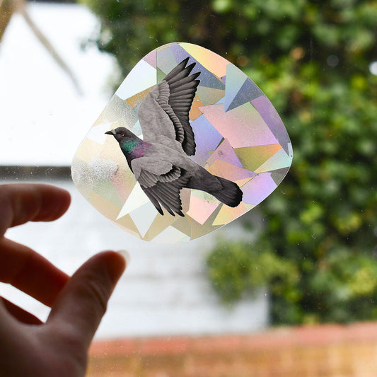 Hand holding a suncatcher decal with a bird design against a blurred outdoor background
