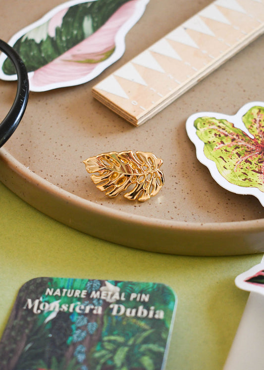 Gold leaf-shaped metal pin on a ceramic tray with nature-themed cards and leaves.