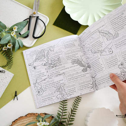 Open book with nature-themed coloring pages on a green surface with plants and scissors.