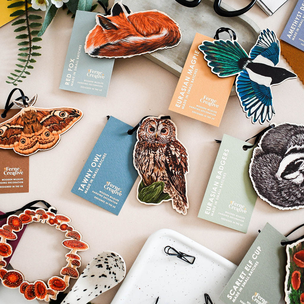 collection of british wildlife wooden hanging decorations including fungi, moths, tawny owl, red fox, badger and magpie with their swing tags