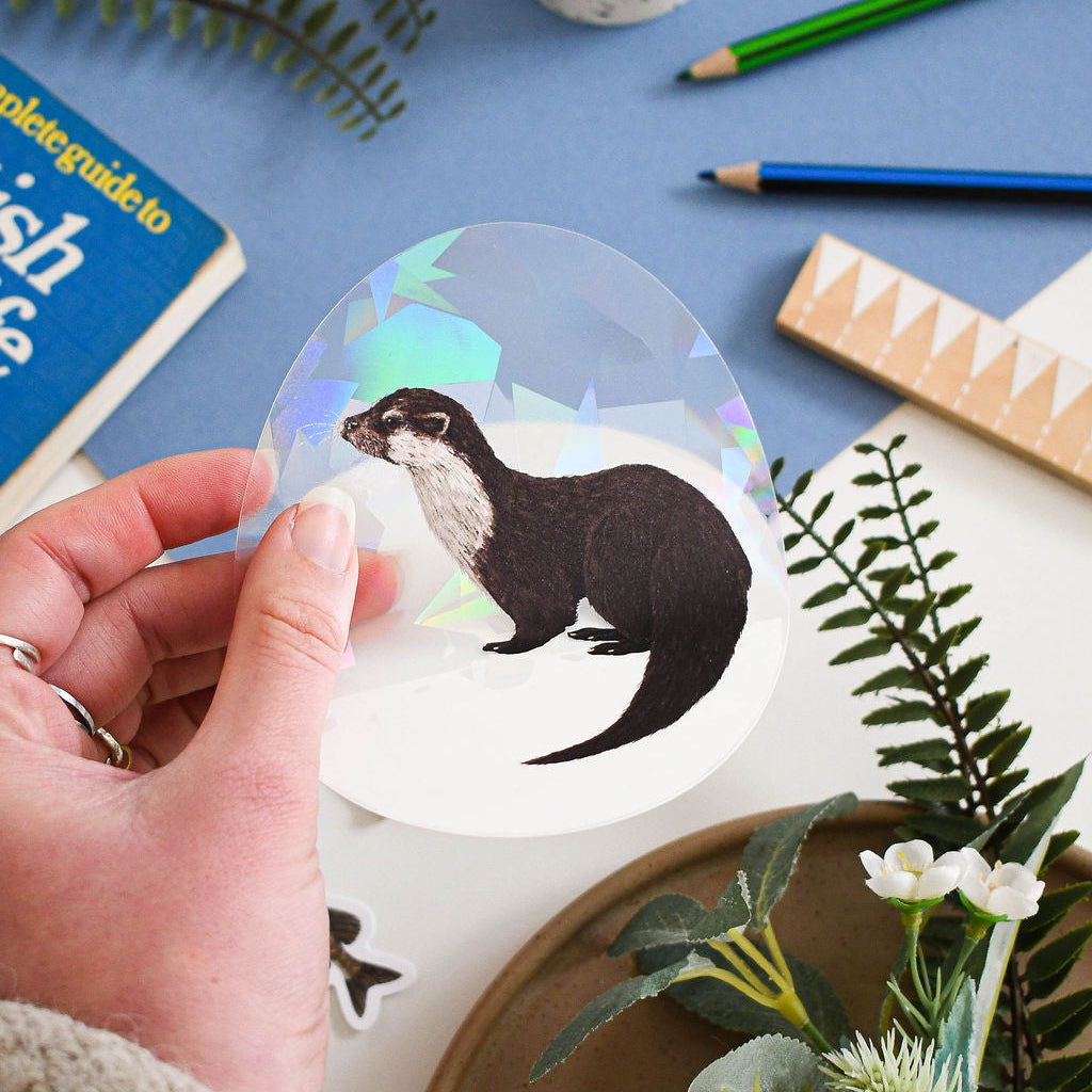 Eurasian Otter rainbow suncatcher decal held over blue background