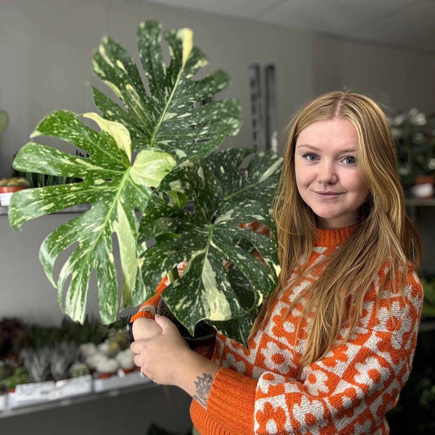 Ferne Creative holding a large leafy plant in an indoor setting