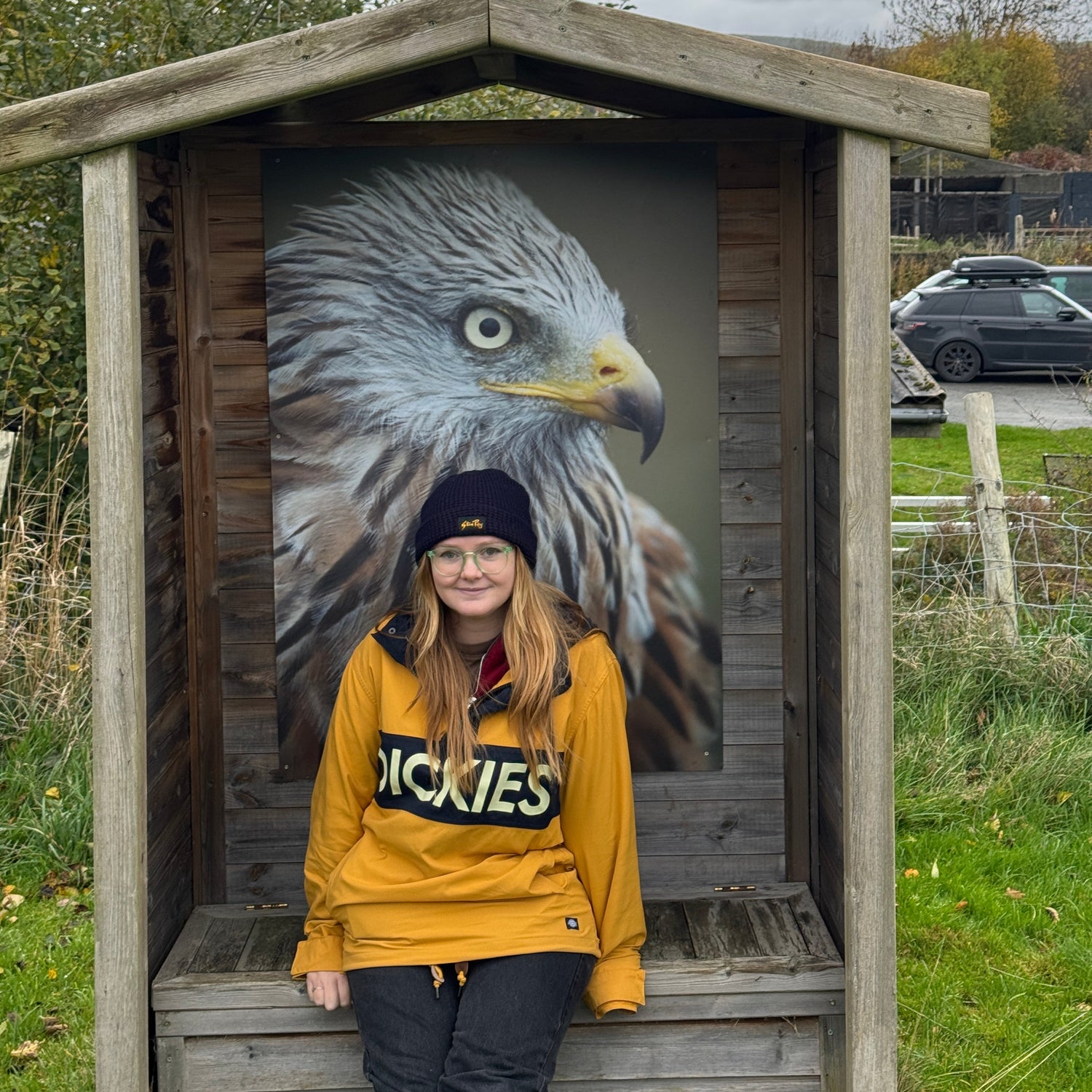 Ferne wearing a yellow jacket with a large Red Kite image on a wooden platform.