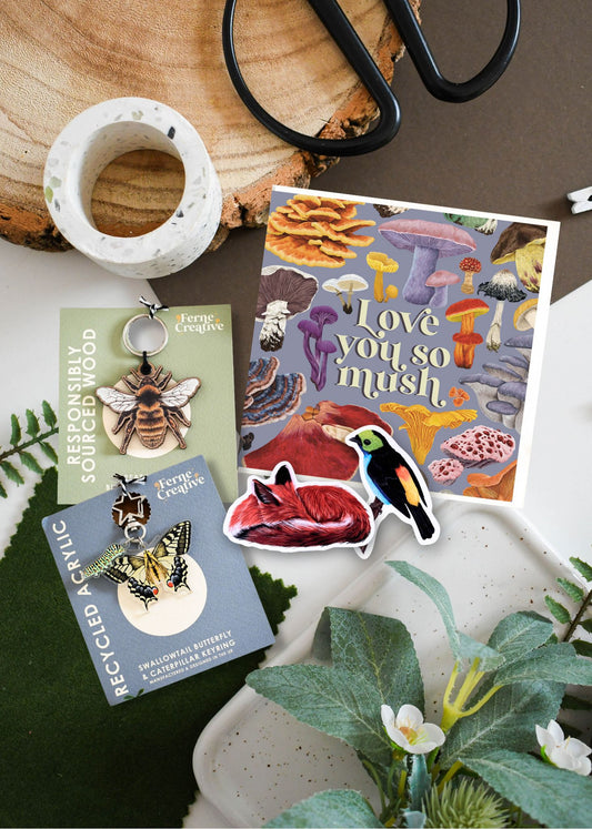 Collection of nature-themed products including cards, stickers, and pins on a wooden surface with plants.