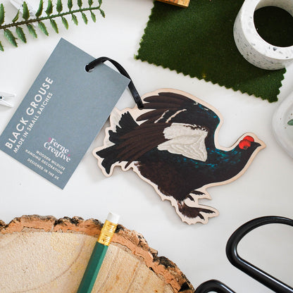 Wooden ornament of a black grouse with a tag on a white surface with greenery and tools.