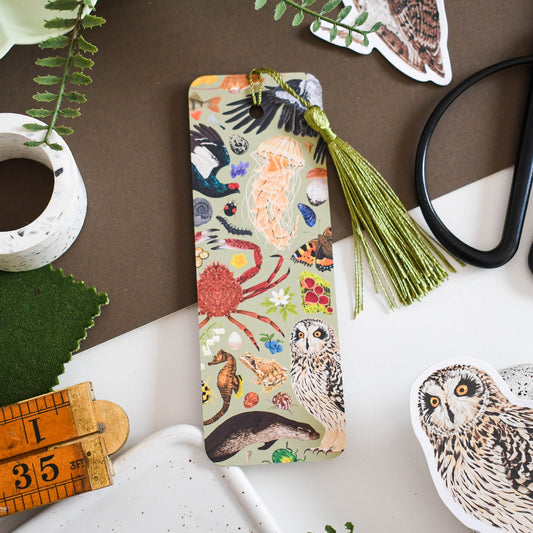 A decorative nature bookmark with tassel on a surface with nature-themed items