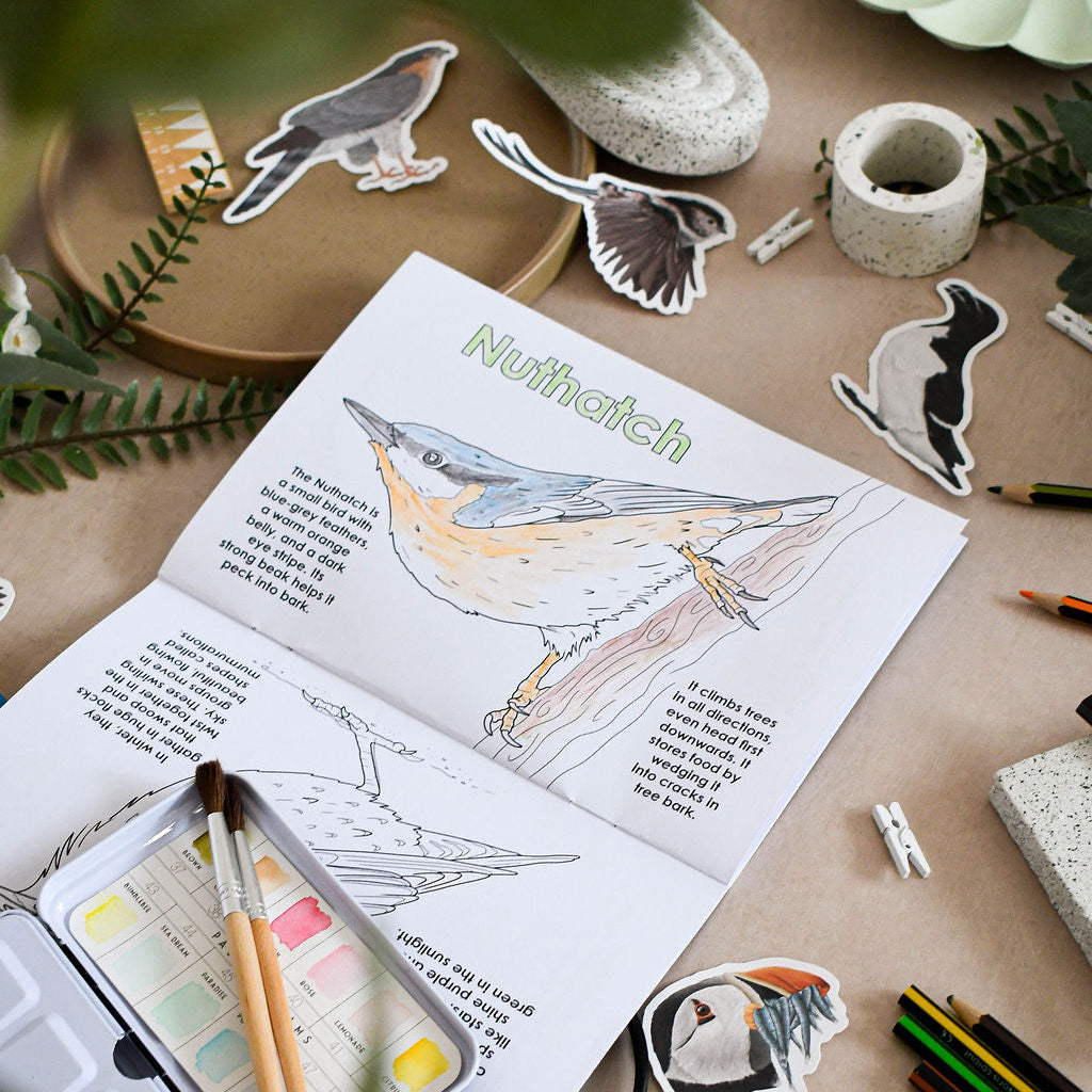 Open book with bird illustration and coloring page on a table with art supplies