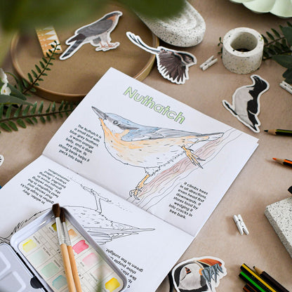Open book with bird illustration and coloring page on a table with art supplies