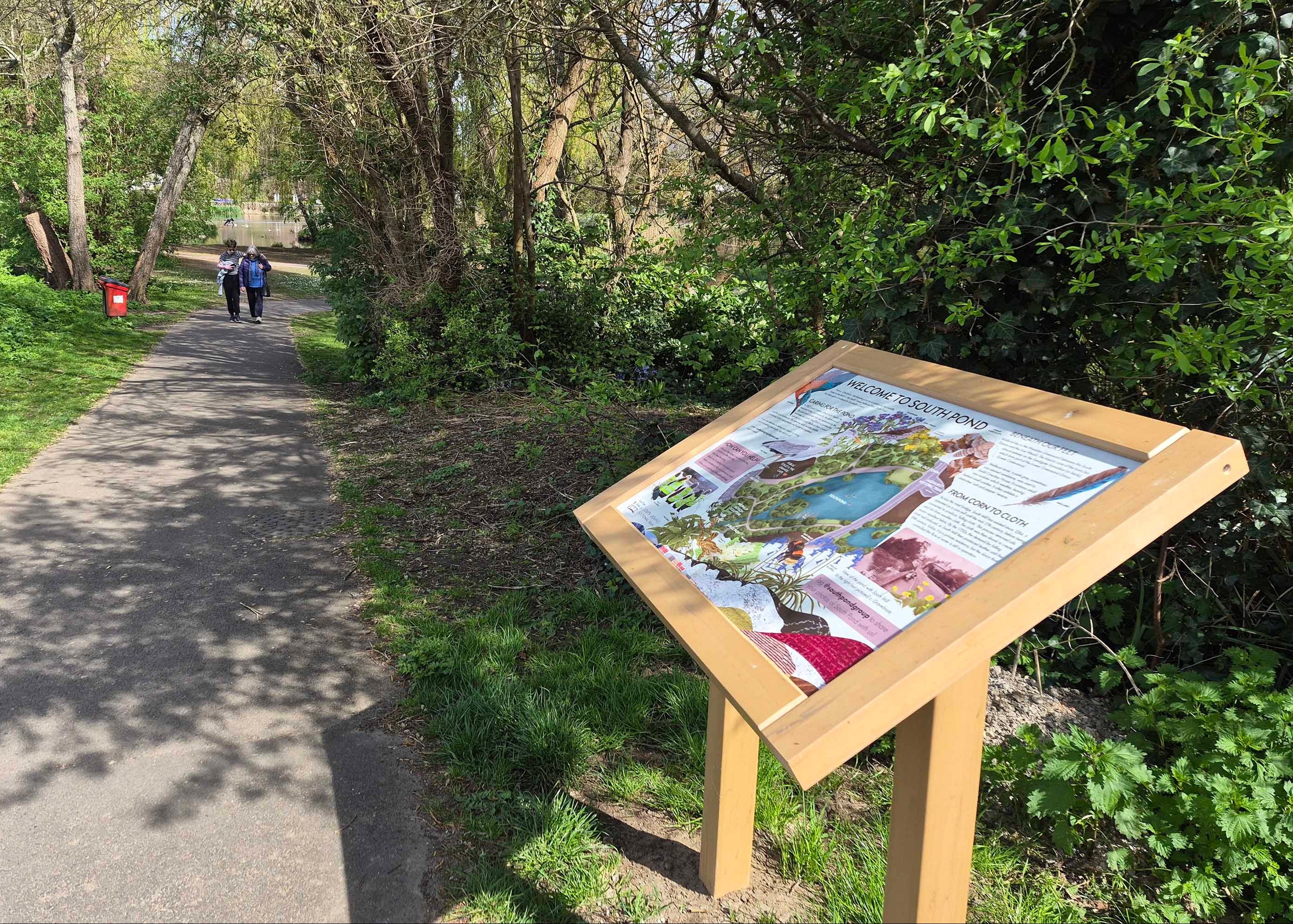 Illustrated Informational sign on a pathway in a park with people walking in the background in South Downs National park